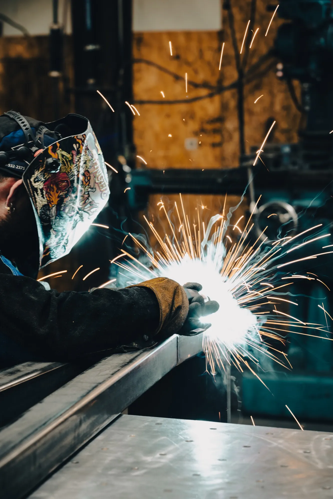 masked worker welding a beam with flashes of light and sparks